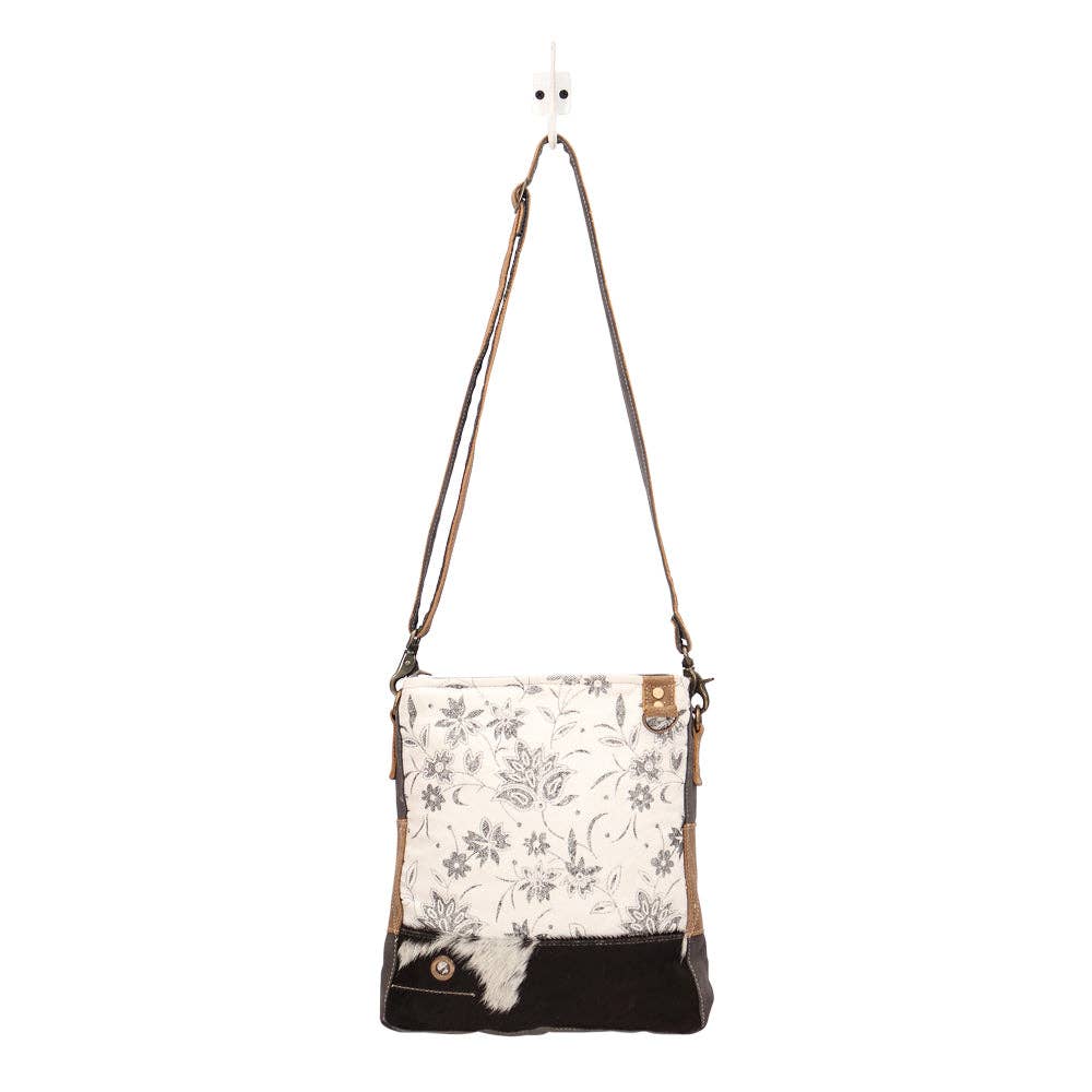 Floral patterned crossbody bag with brown strap on a white background