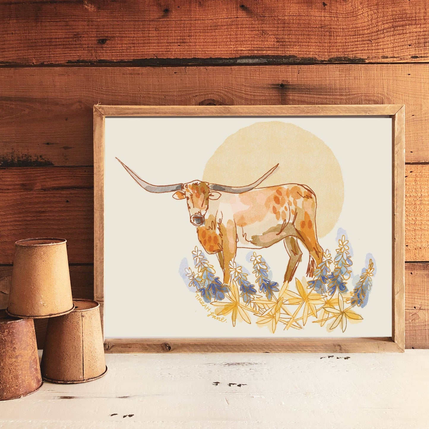 Framed artwork of a longhorn cow with flowers against a wooden wall.