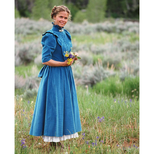 Woman in a Prairie Bustle Old West Dress holding flowers in a scenic field with greenery and wildflowers.