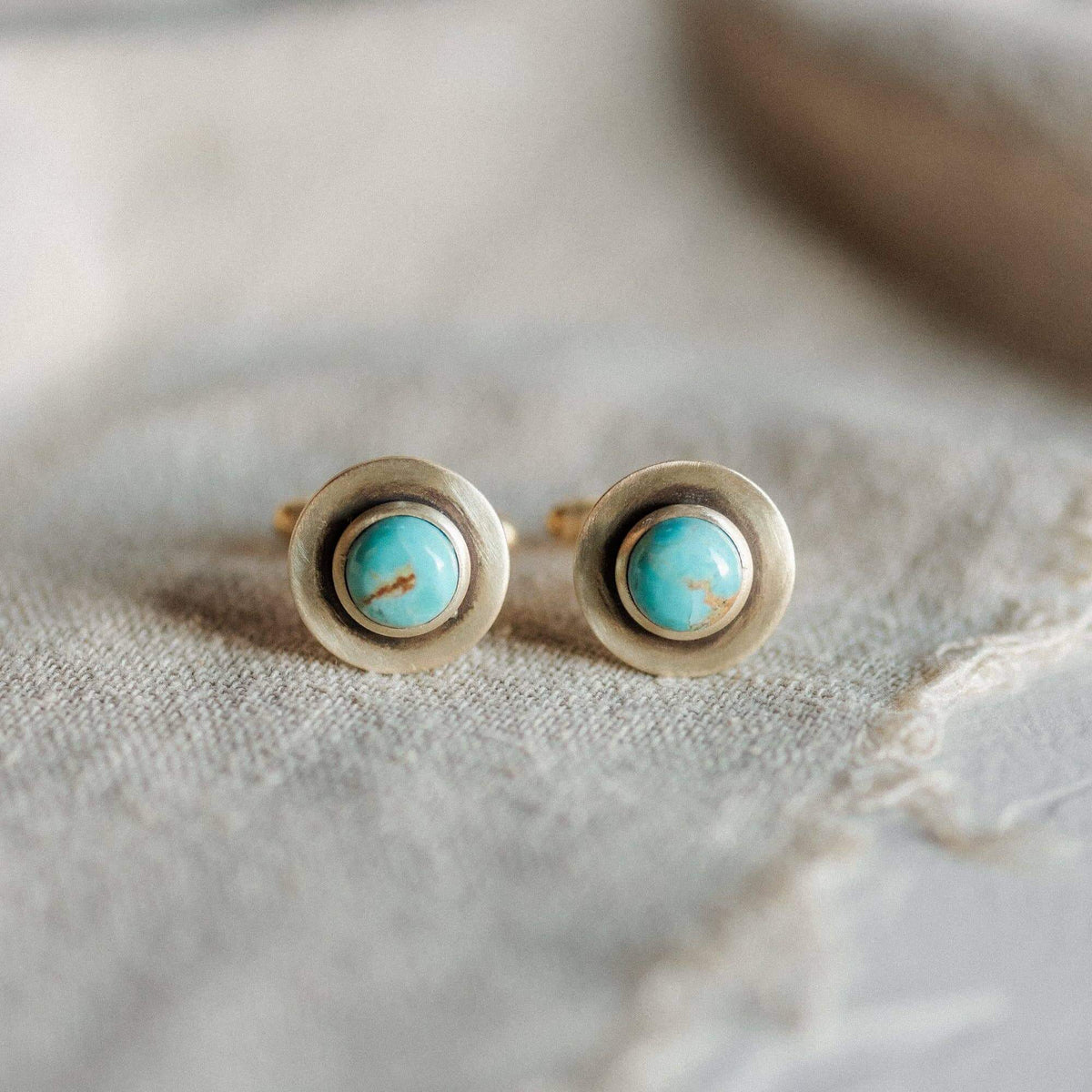 Pair of gold earrings with turquoise stones on a textured beige surface