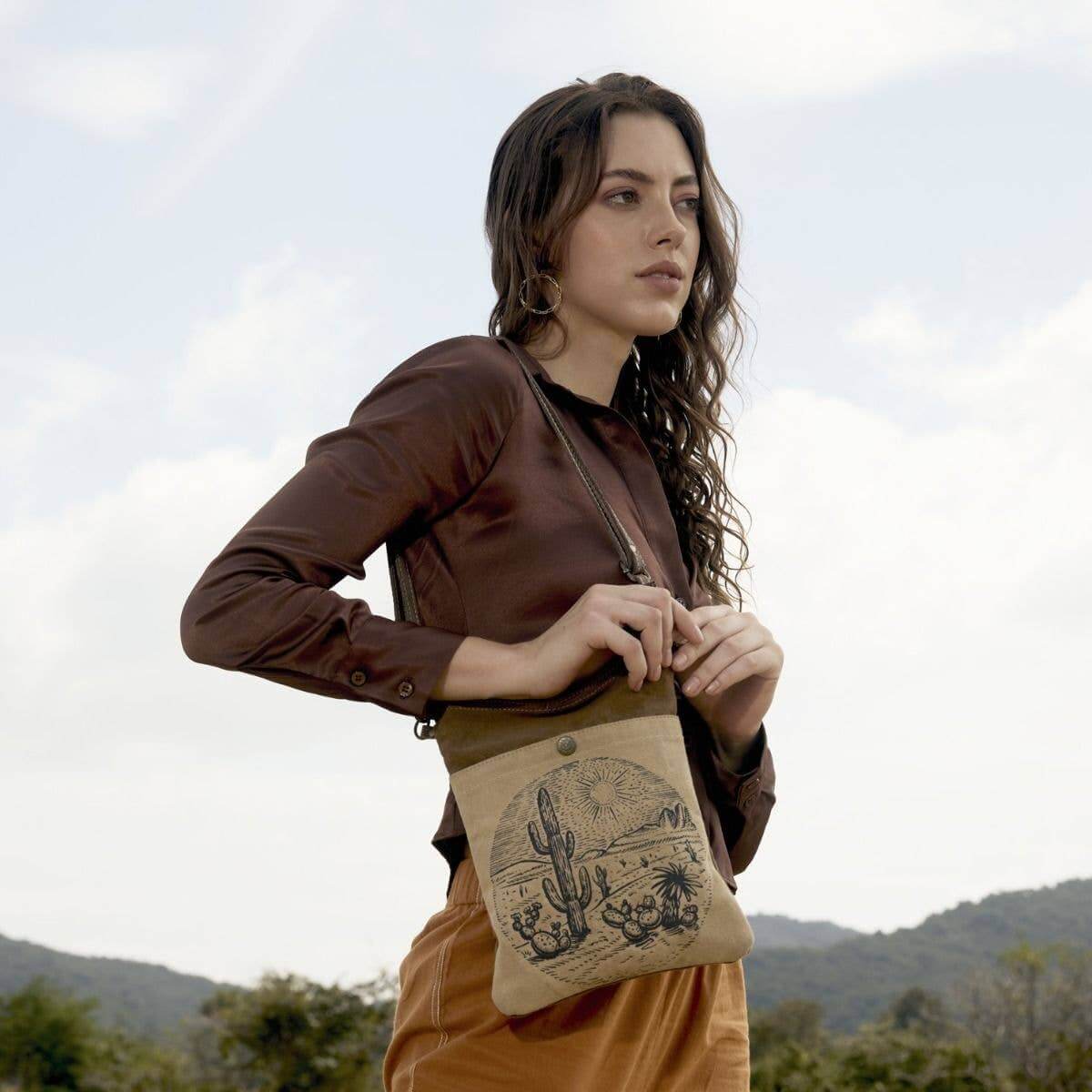 Woman holding a brown leather bag with a desert design outdoors