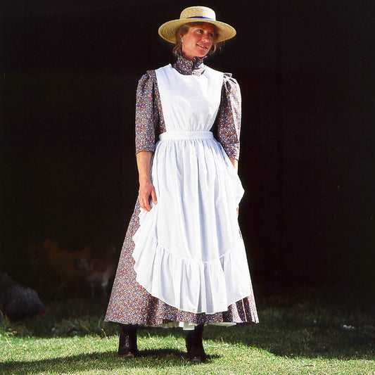 Woman wearing a white chicken feeding country apron over a floral dress, in a barnyard setting.