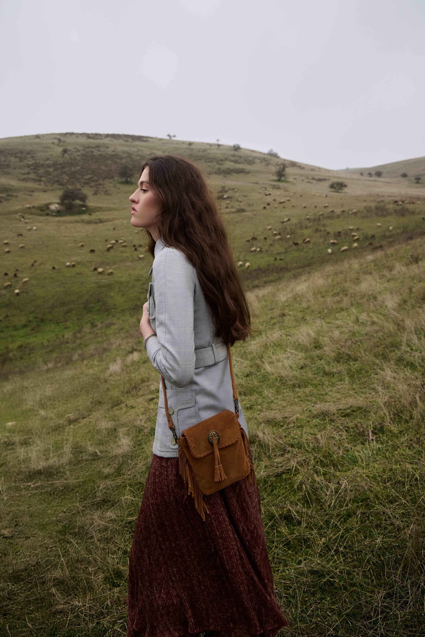 Woman standing in a field with sheep, holding a brown bag