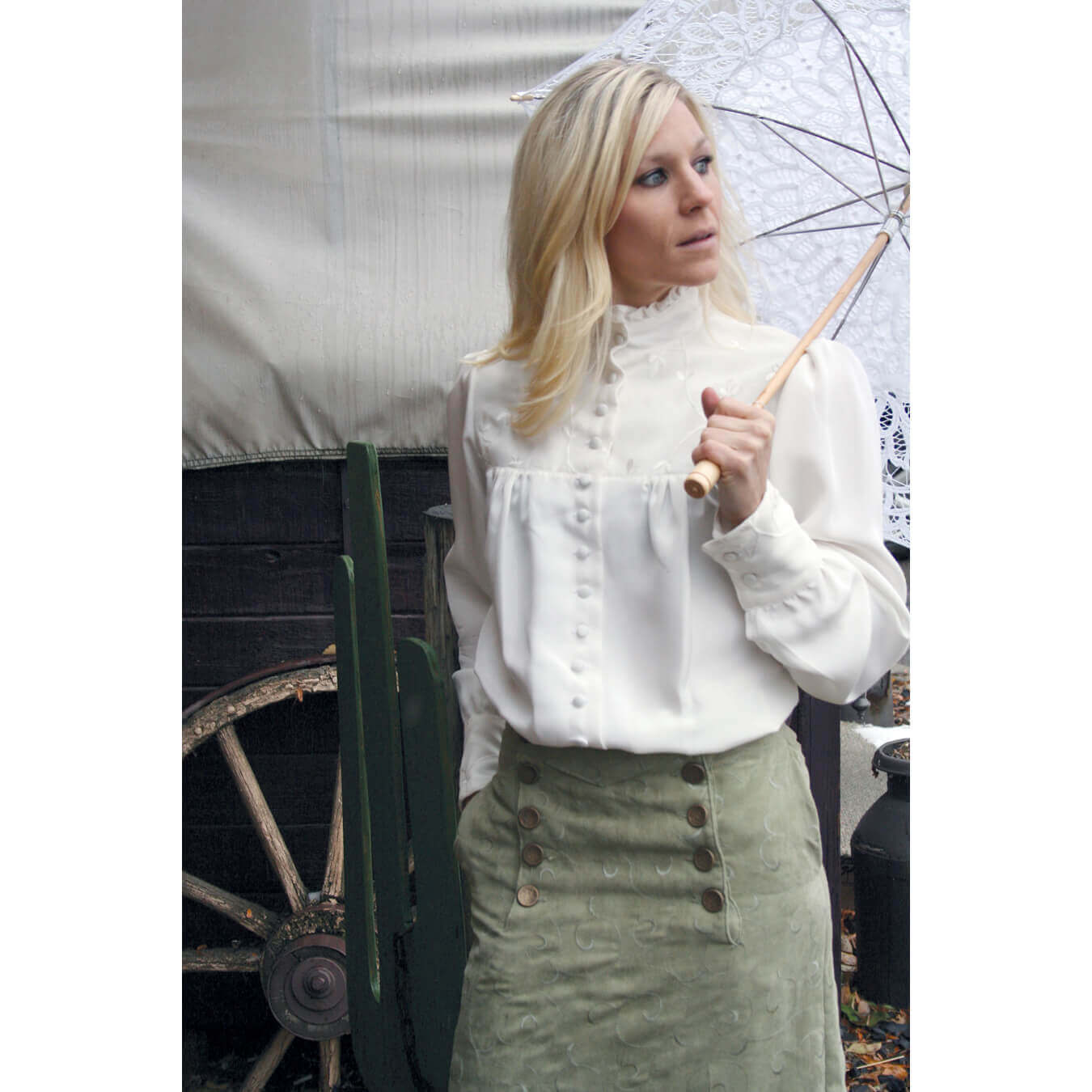 Victorian Laura Blouse in natural silk with ruffled neckline, worn by a model holding an umbrella, paired with a green skirt.