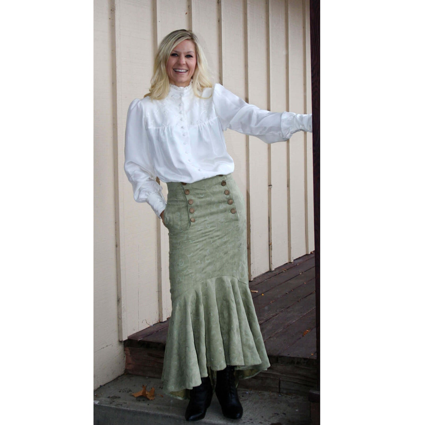 Woman wearing Victorian Laura Blouse with ruffle neck and green flared skirt, posing outdoors.
