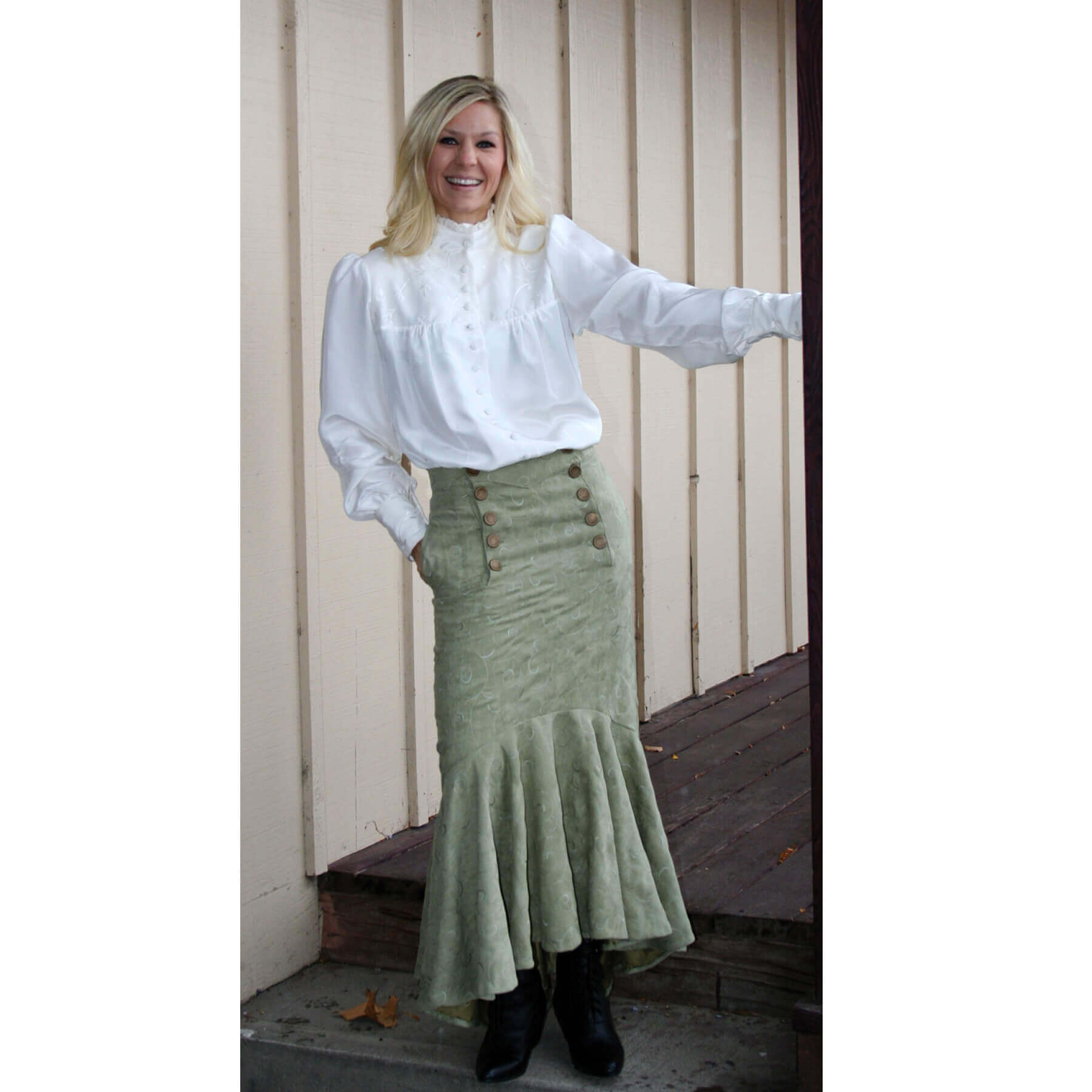 Woman wearing Victorian Laura Blouse with ruffle neck and green flared skirt, posing outdoors.