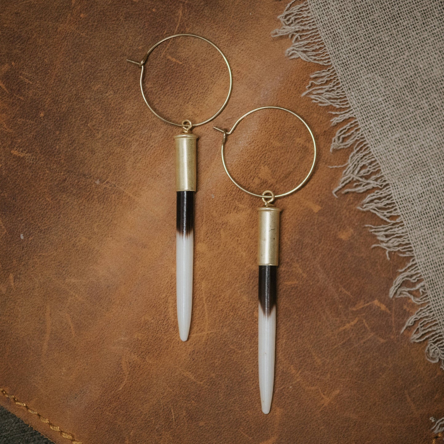 Pair of hoop earrings with cylindrical pendants on a textured brown surface