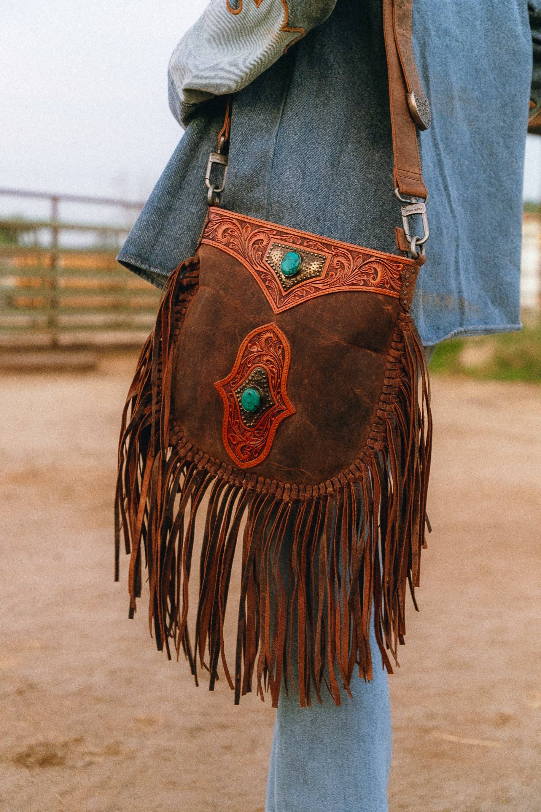 Brown leather fringe bag with turquoise stones held by a person in an outdoor setting.