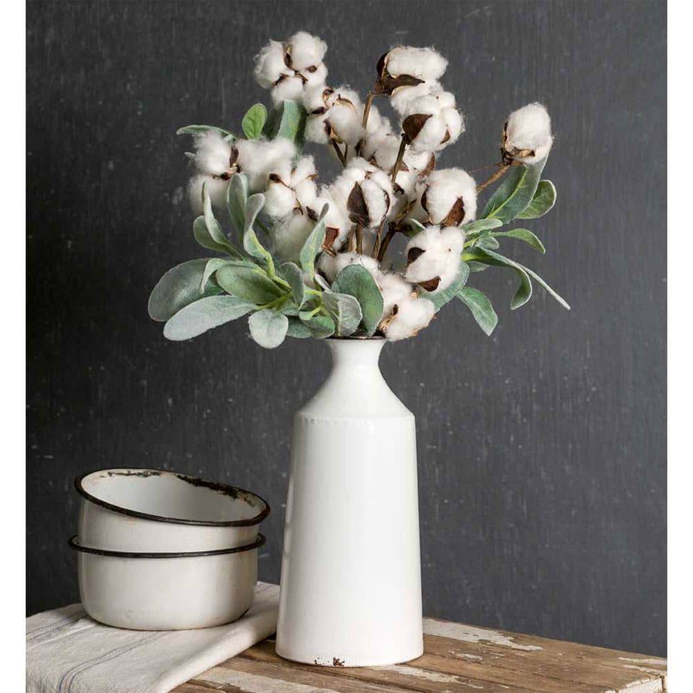 White vase with cotton-like flowers on a wooden surface against a dark background