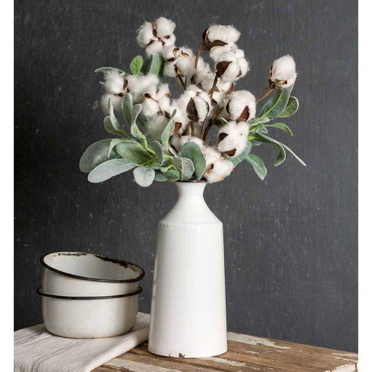 White vase with cotton-like flowers on a wooden surface against a dark background