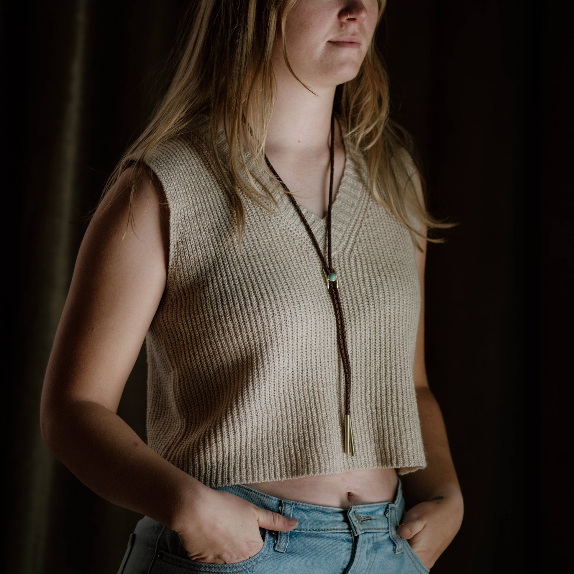 Woman wearing a beige knitted vest  with bolo tie against a dark background