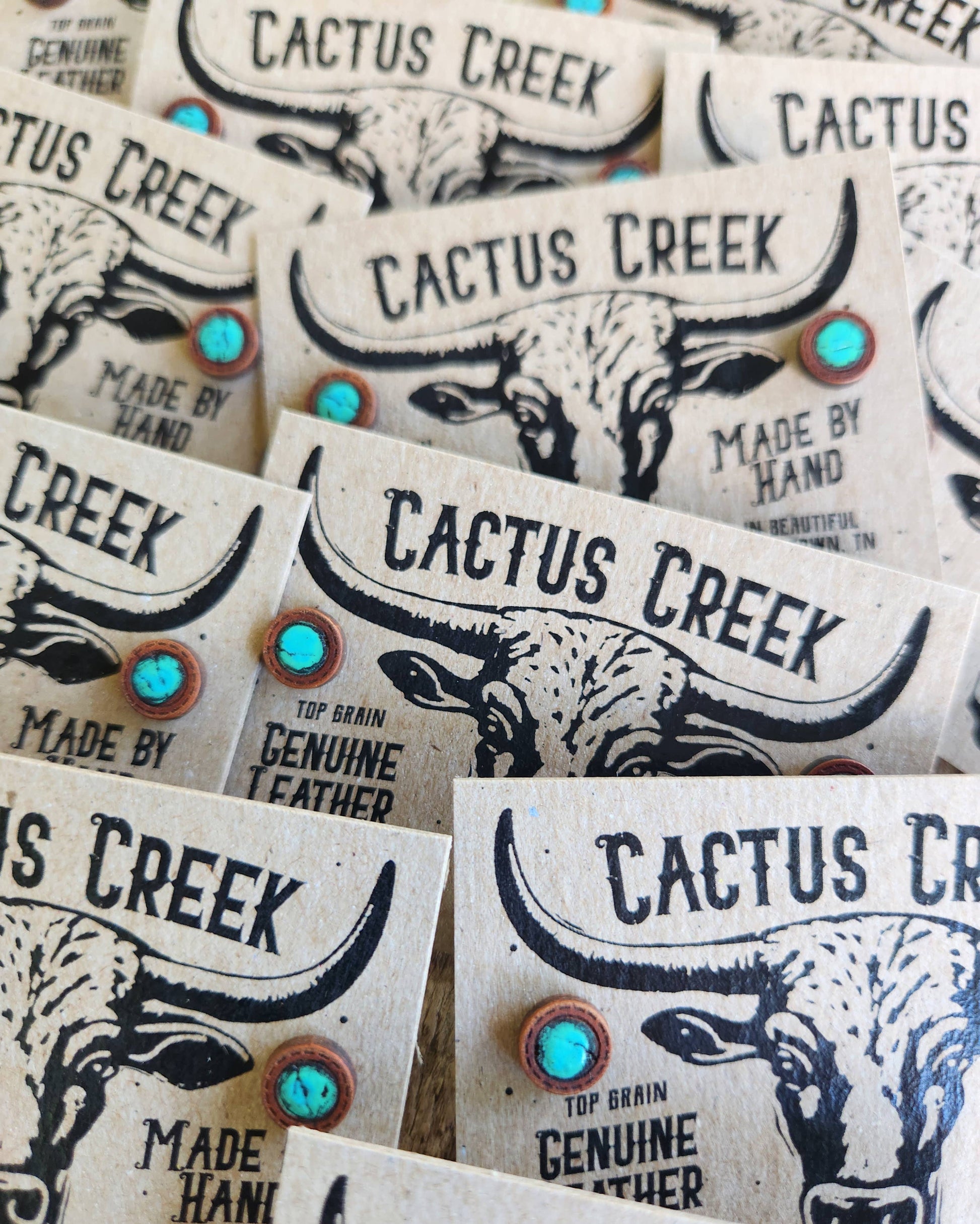 Close-up of 'Cactus Creek' branded earrings with turquoise stones and bull designs.