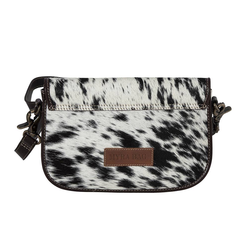 Black and white cow print crossbody bag with a brown leather patch on a white background