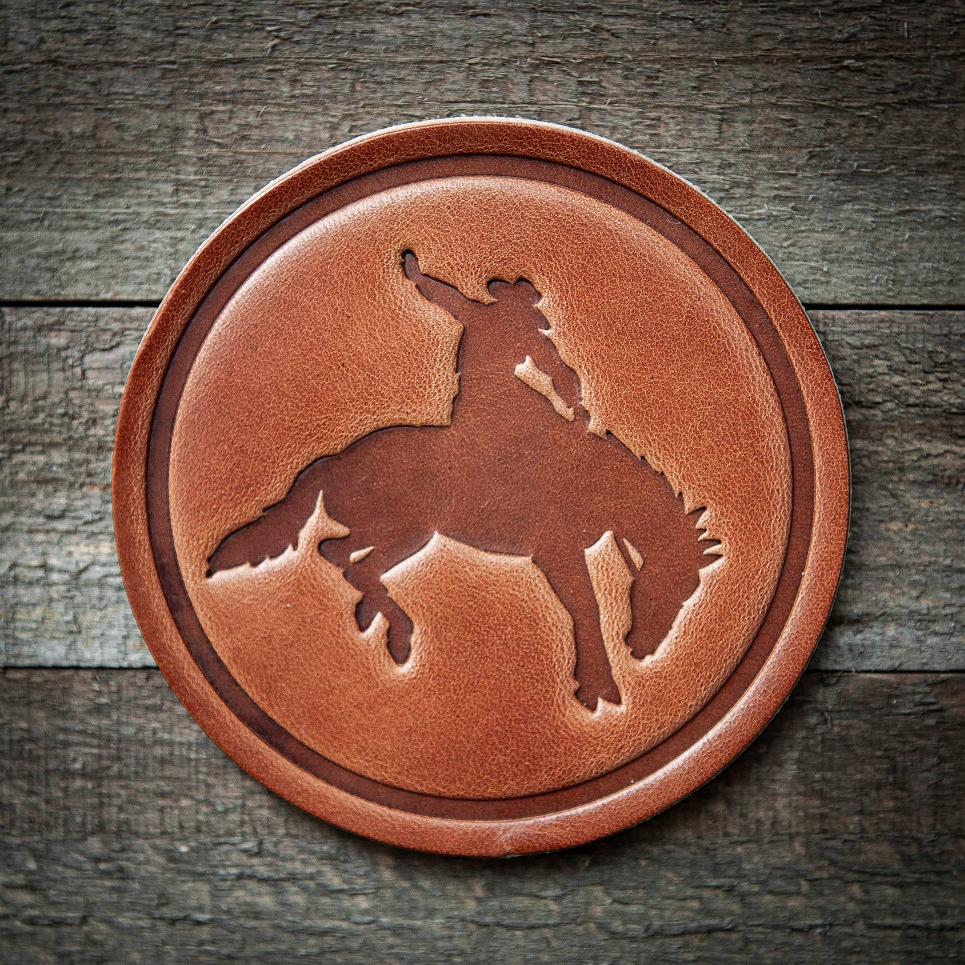 Round leather coaster with a horse and rider design on a wooden background