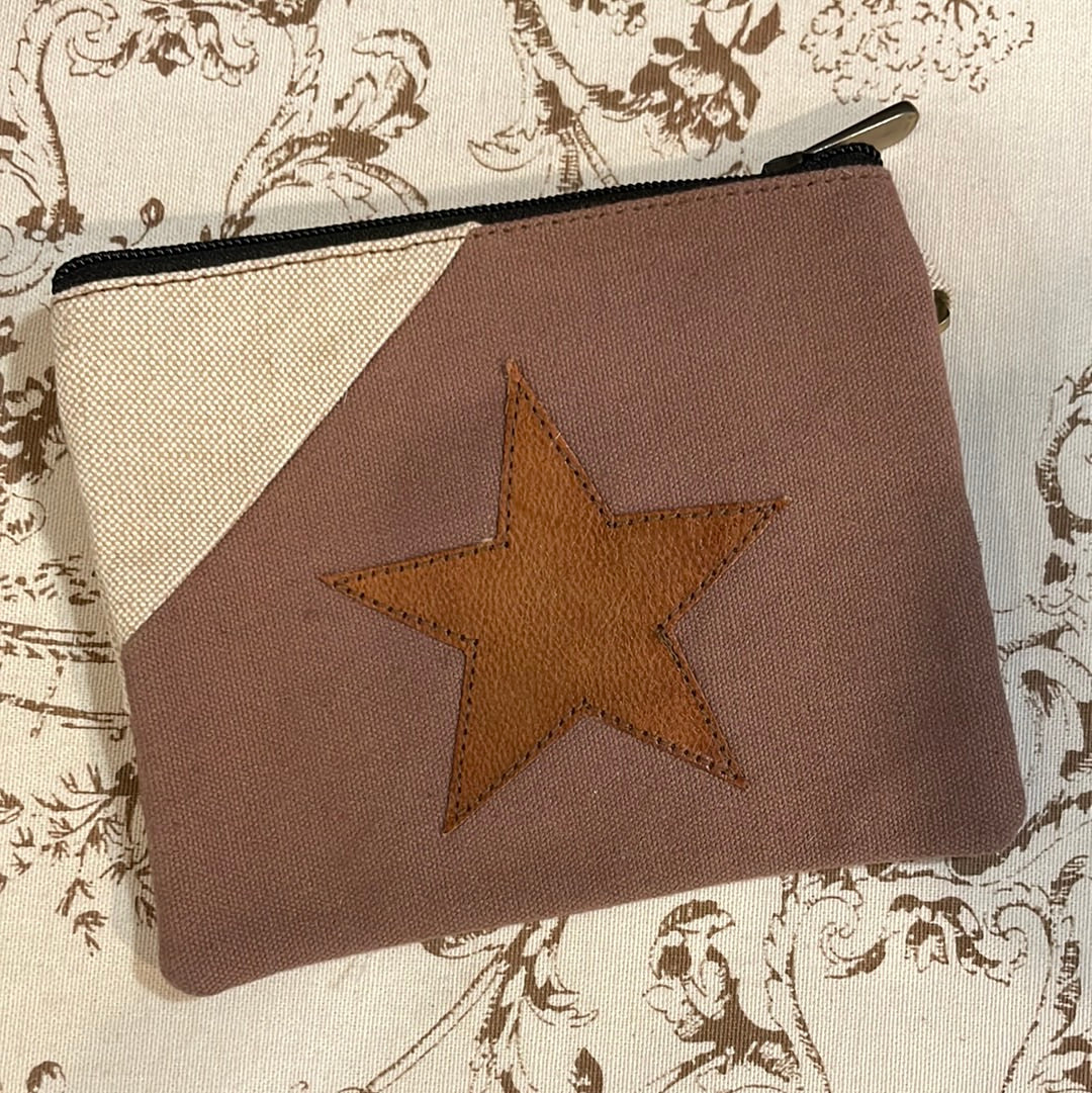 A brown wristlet wallet with a star-shaped embossment on the front, placed on a textured fabric background.