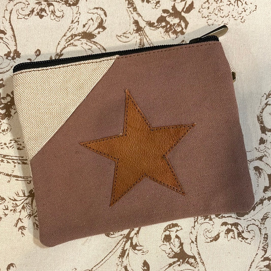 A brown wristlet wallet with a star-shaped embossment on the front, placed on a textured fabric background.