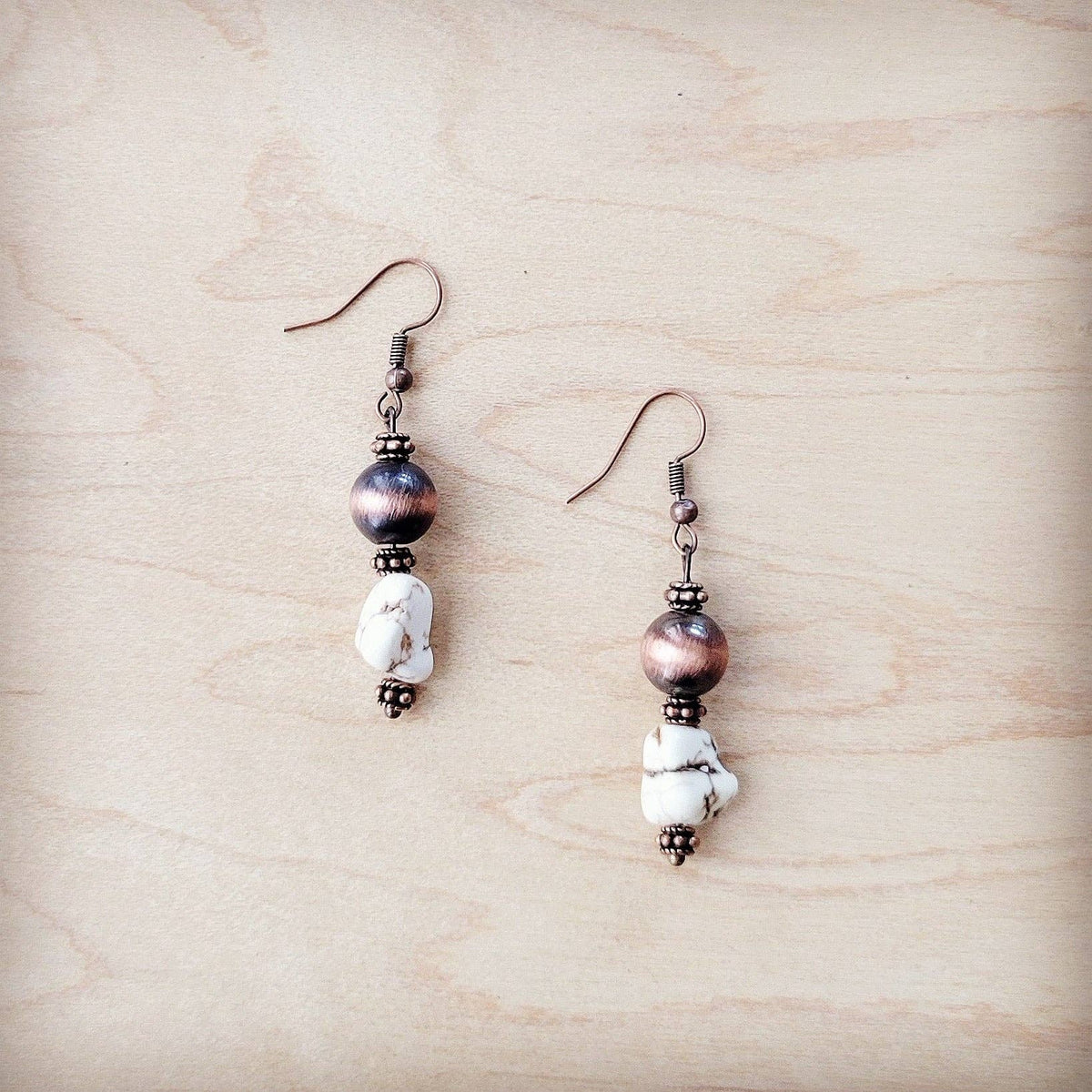 Pair of earrings with copper and white beads on a wooden surface