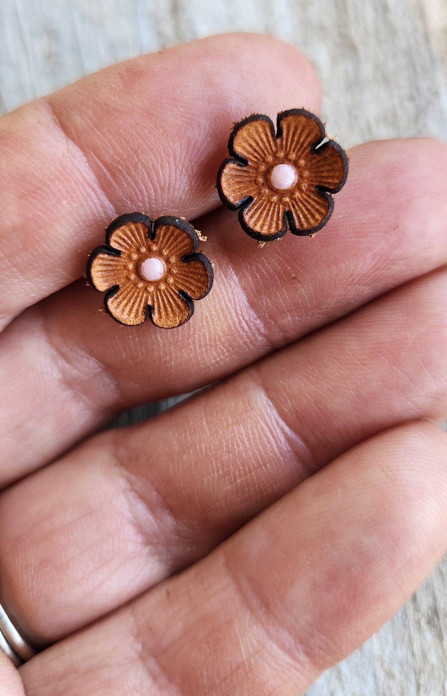 Flower-shaped earrings held between fingers on a neutral background
