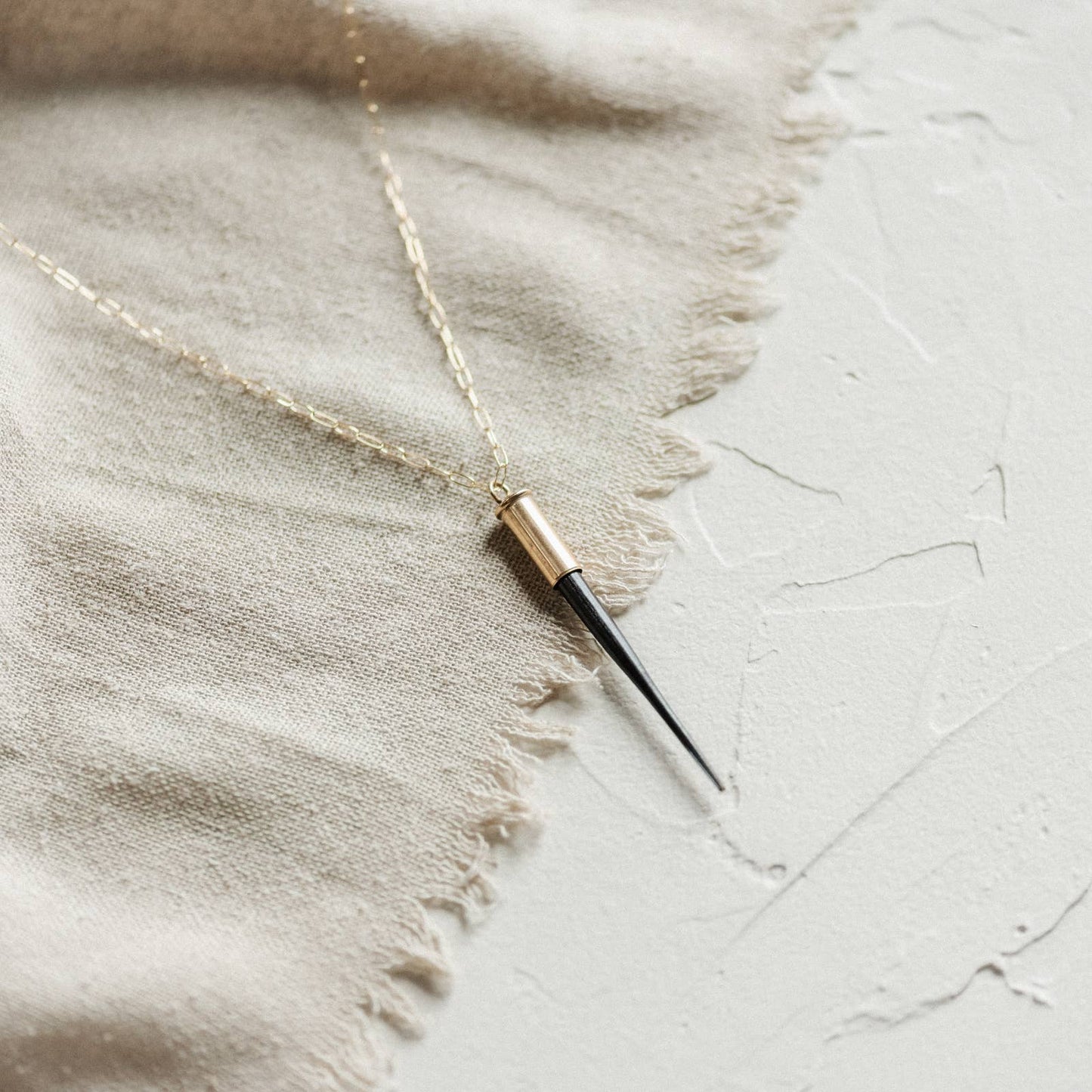 Necklace with a cylindrical pendant on a textured fabric background