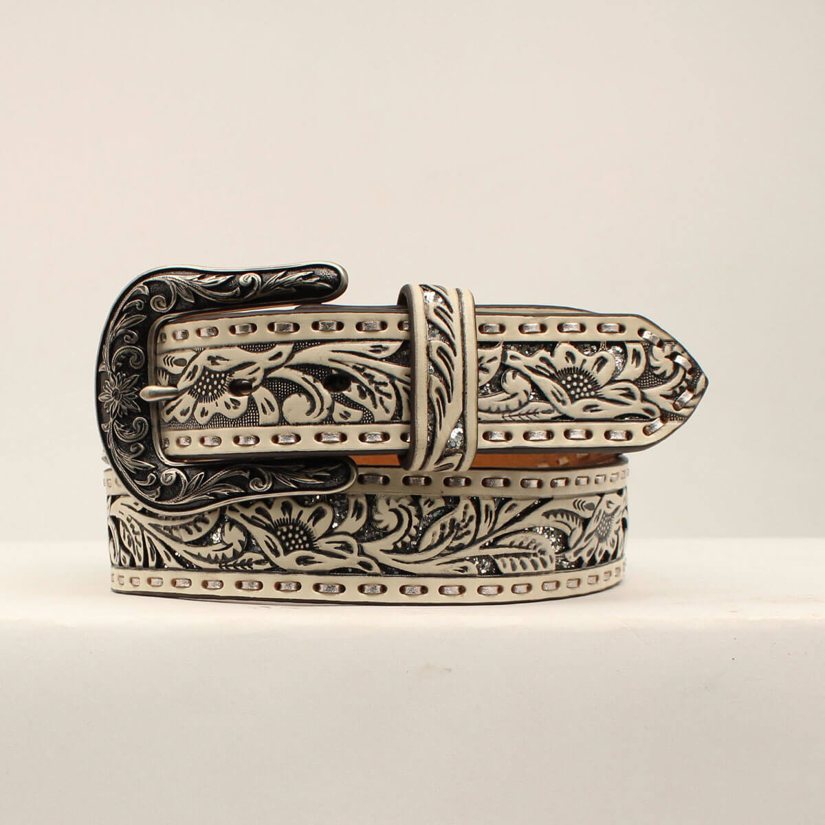 This gorgeous ladies Ariat belt has country roots with a modern flair. It features a white floral embossed piercing with silver glitter underlay and silver laced edges. It is finished with a beautifully detailed buckle. This quality belt will look good with any outfit, and will easily be your favorite.