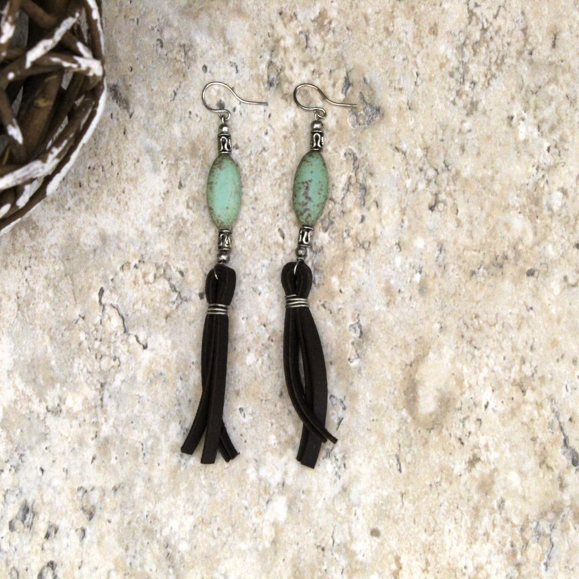Pair of earrings with green beads and black tassels on a textured surface