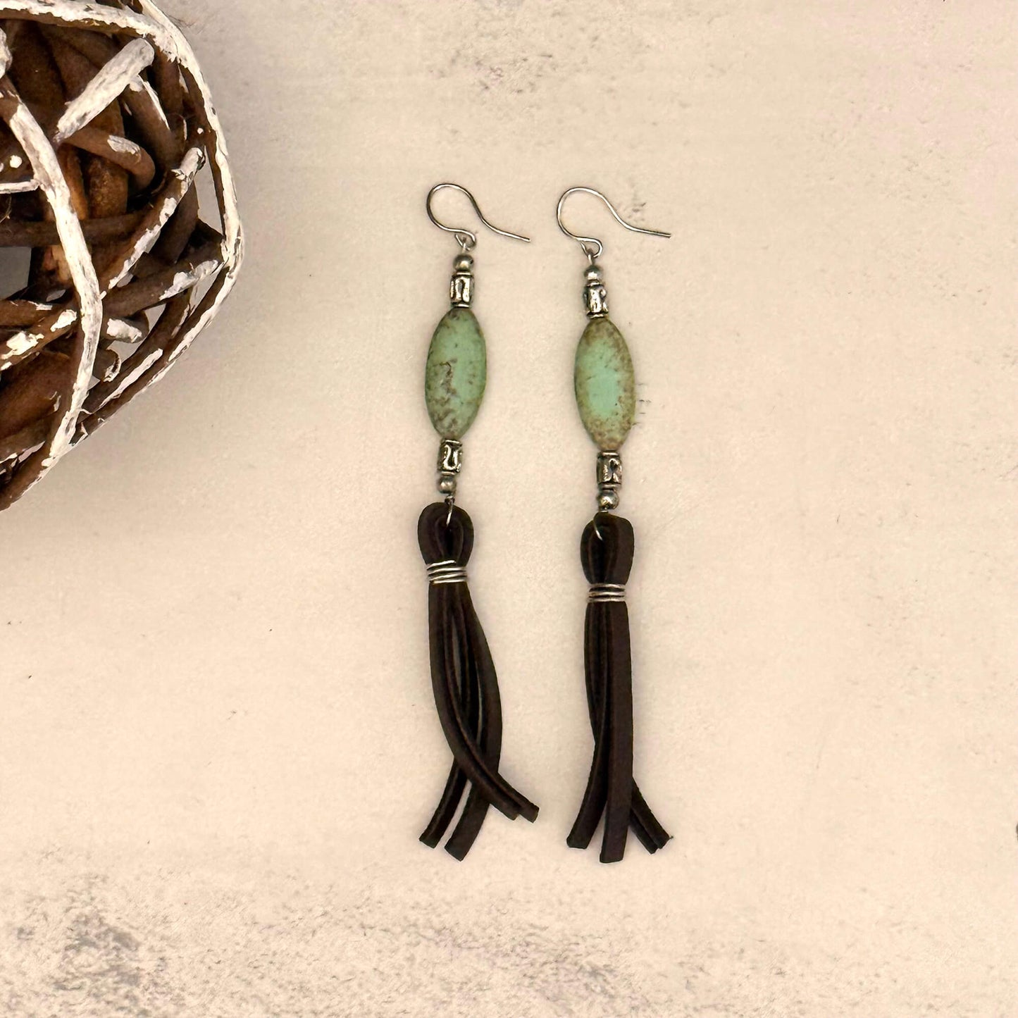Pair of earrings with green beads and black tassels on a textured surface.