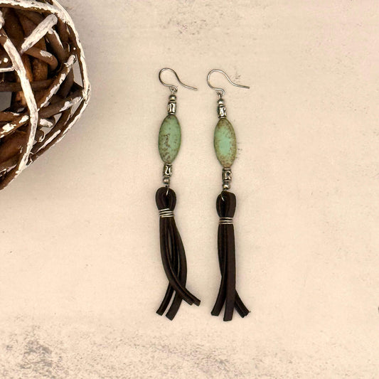 Pair of earrings with green beads and black tassels on a textured surface.