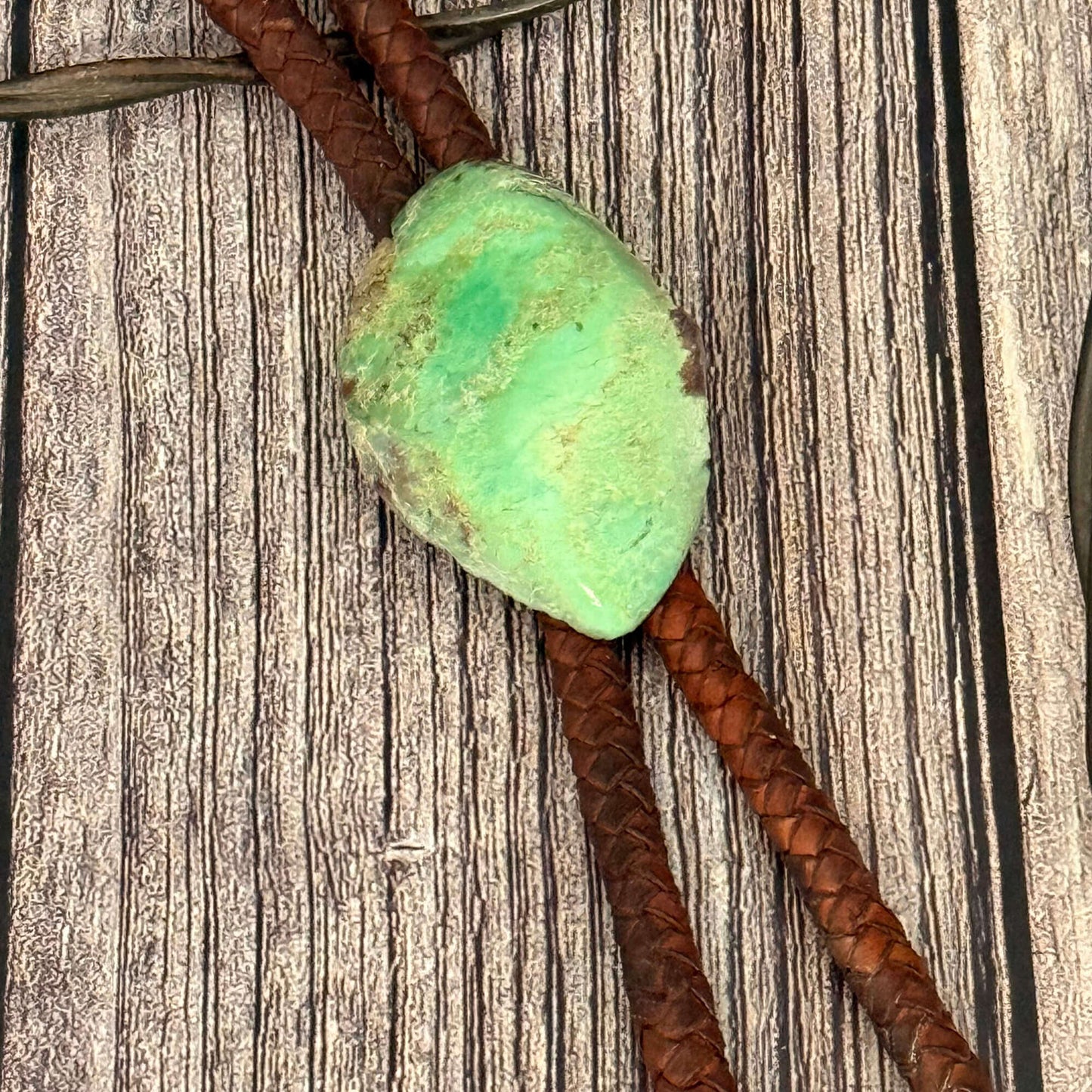 Turquoise stone on a brown leather cord against a wooden background