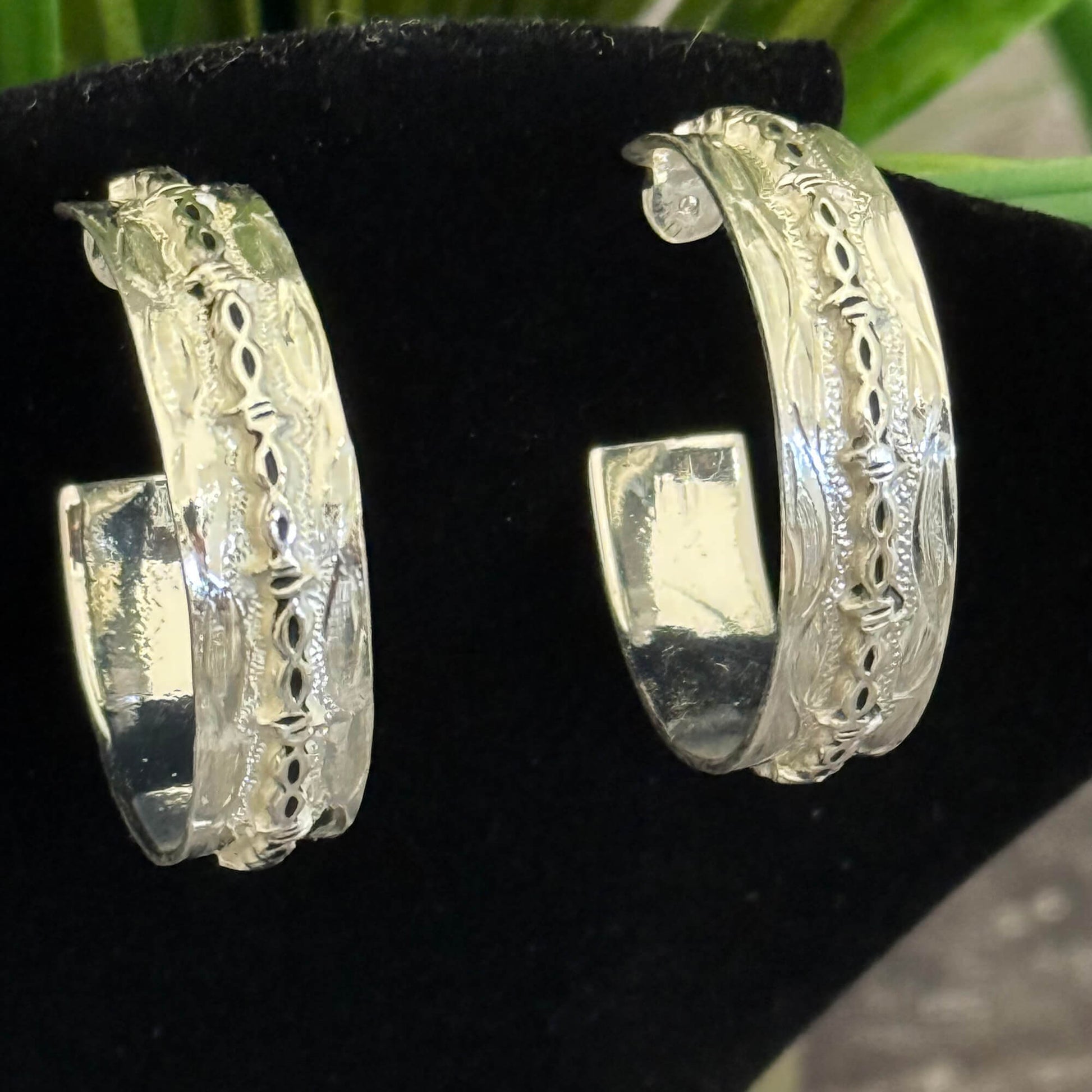 Silver hoop earrings with intricate designs on a black stand.