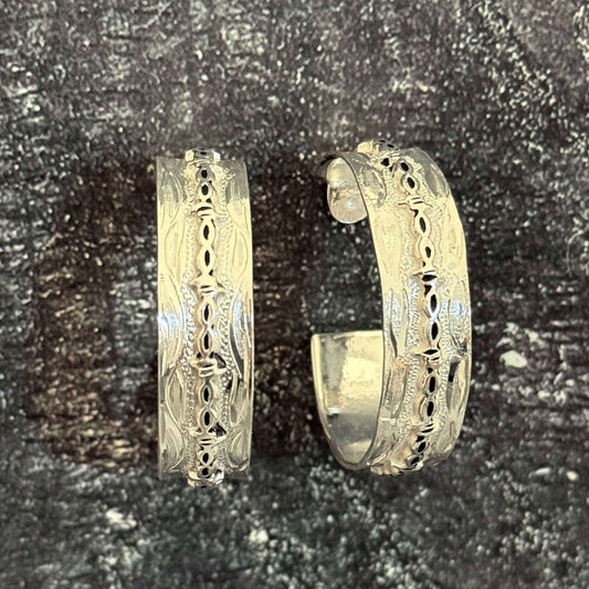 Pair of gold hoop earrings with intricate designs on a dark textured background