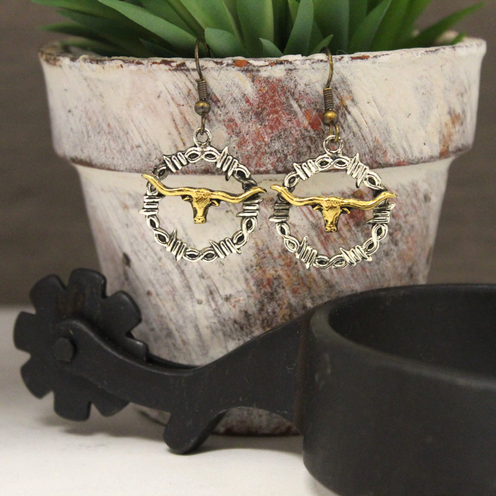 A gold longhorn silhouette in the center of a round silver barbed wire design. Earrings come on a wire hooks that hang about 1-1/2" long and circle measures 1" diameter. Imported.