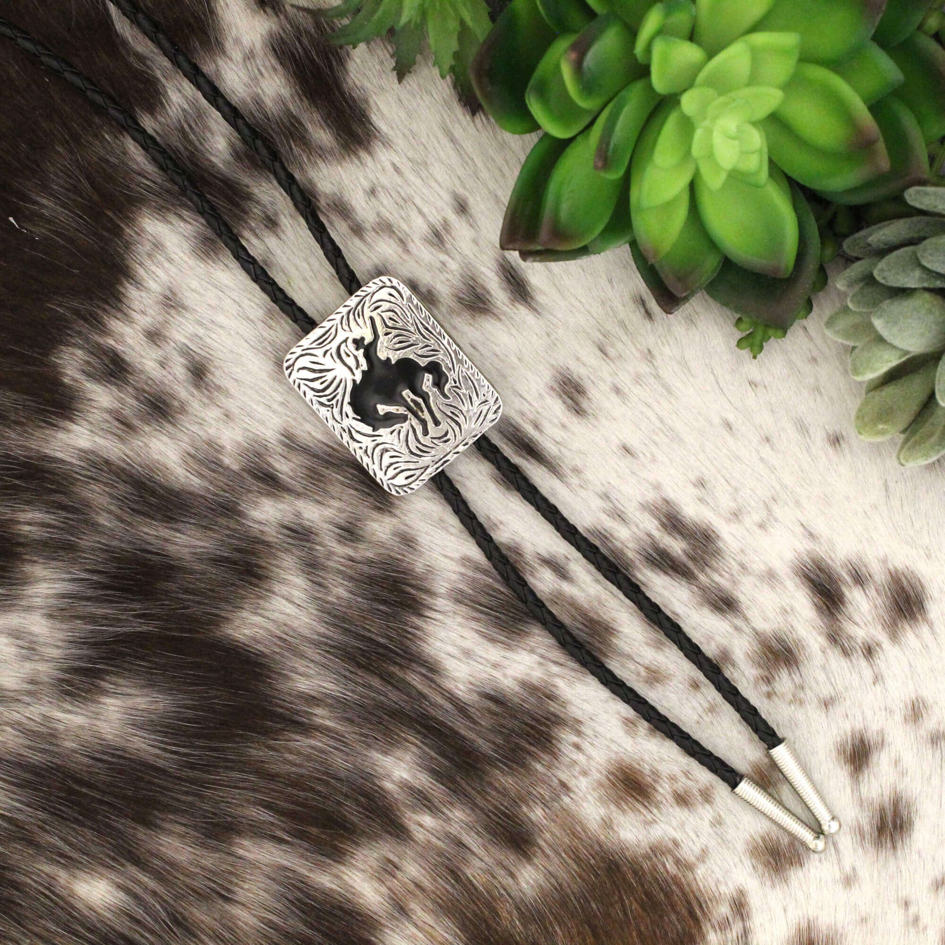 The centerpiece of this bolo tie is a stunning silver buckle adorned with a classic buckaroo bronc silhouette, capturing the spirit of the Wild West. The black cord is not only durable with elegant silver tips that add a touch of refinement. Embrace your inner cowboy and showcase your unique style with this timeless piece that seamlessly blends tradition with modern elegance.
