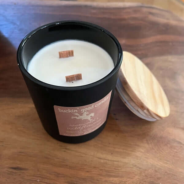 Candle in a black container with a wooden lid on a wooden surface