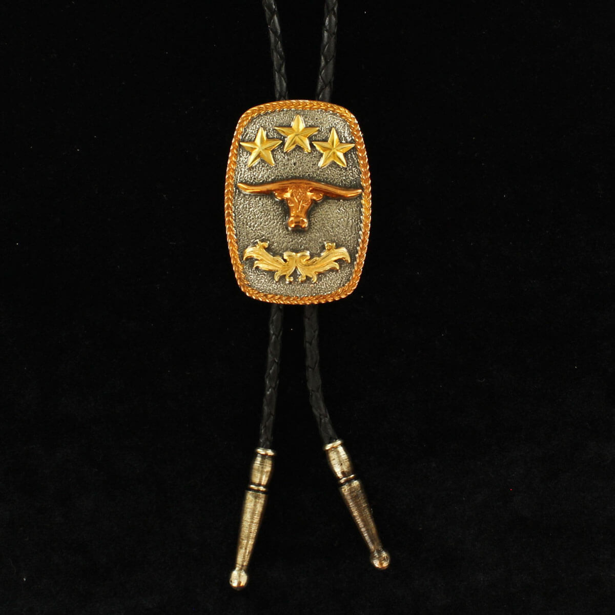 The rectangle bolo features a longhorn motif on an antiqued silver bolo with copper braided trim and gold floral and star accents with a black leather braided cord. Both measure 38” long with antiqued silver tips.