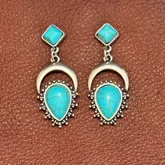 Turquoise stone earrings with silver detailing on a brown textured background