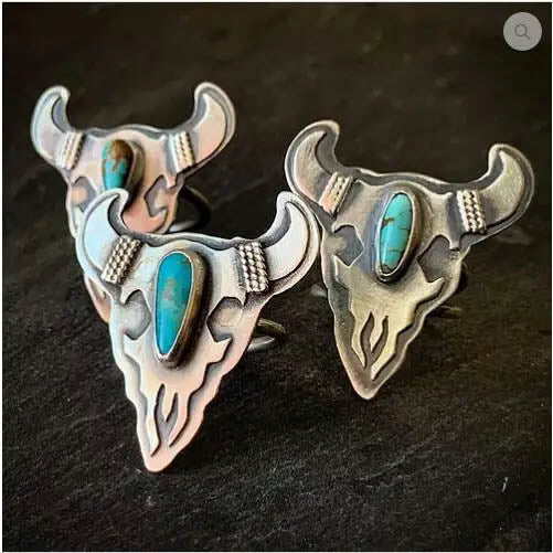 Each of these sterling silver ring features a different piece of American Turquoise, known for its color ranges of blues, greens, browns and blacks. The cattle skull image is an original drawing, sawn out of sheet metal by hand, with all the the designs elements then soldered together in layers. Material: Sterling silver, American Turquoise. Size: Each ring measures approximately 1.5" in length, and 1 3/8" across at its widest point.