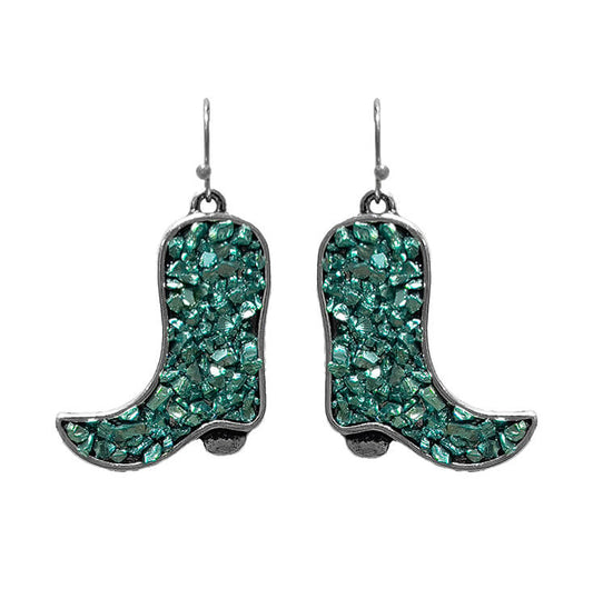 A pair of dangling cowboy boot earrings covered in sparkling green glass chips with silver-tone metal borders and hooks, shown on a plain white background.