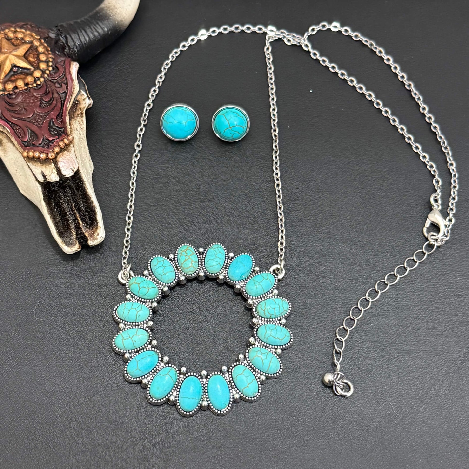 Turquoise necklace and earrings on a dark surface with a cow skull.