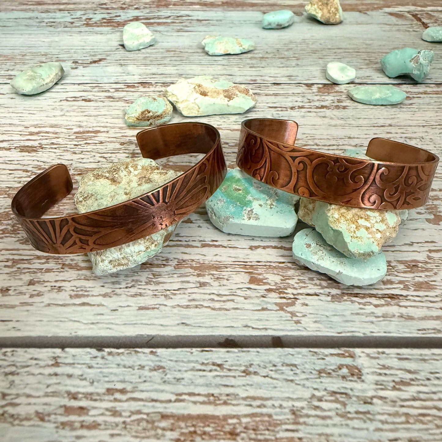 Two copper bracelets on a wooden surface with turquoise stones.