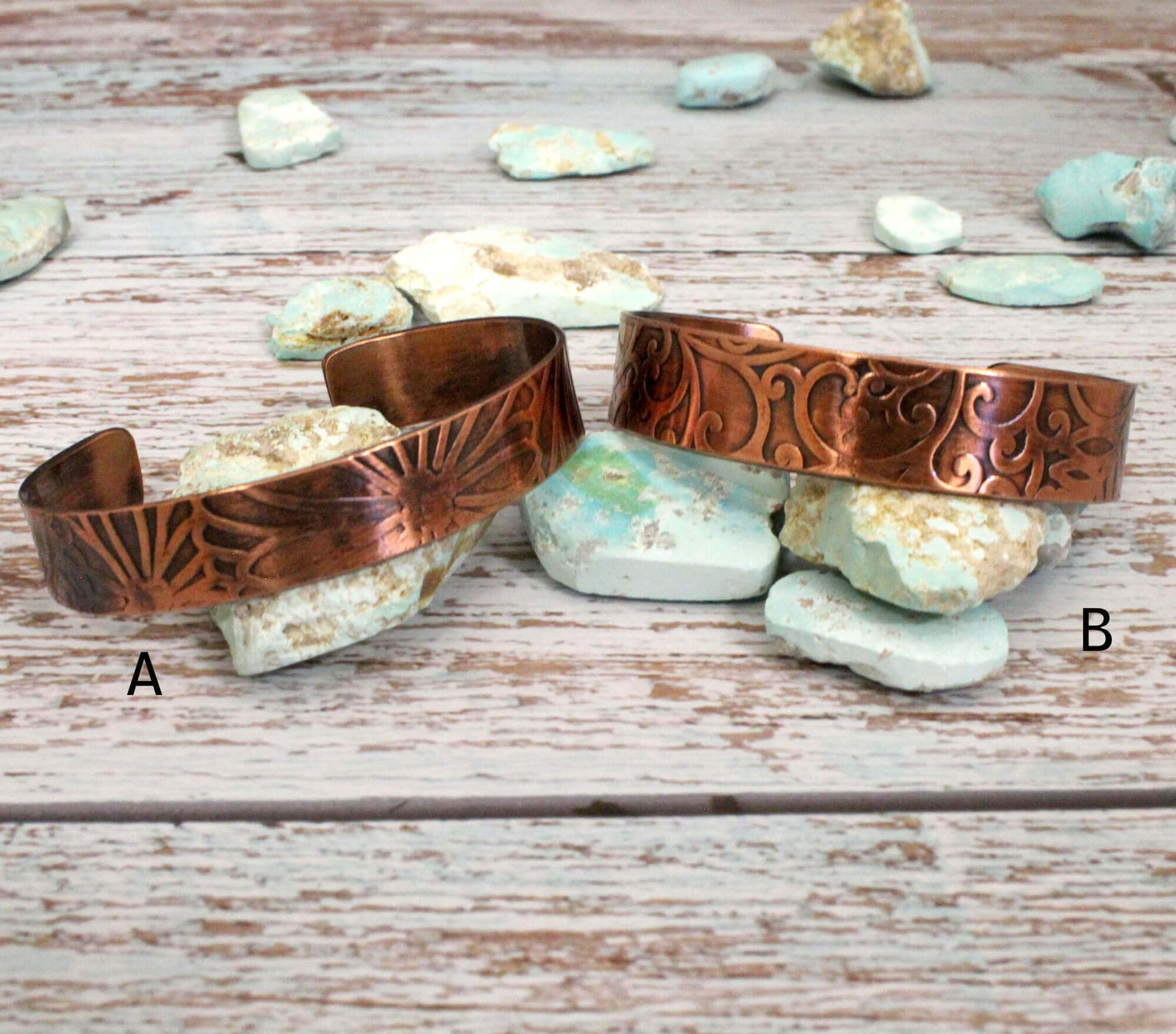 Two copper bracelets on a wooden surface with stones