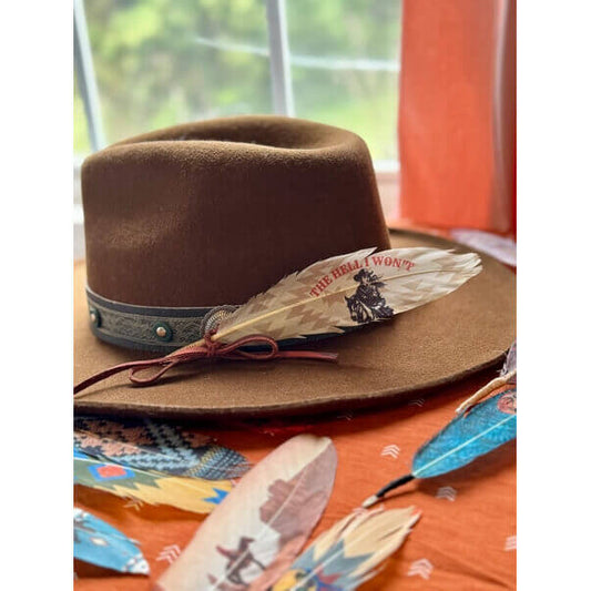Brown cowboy hat with decorative feather on an orange surface