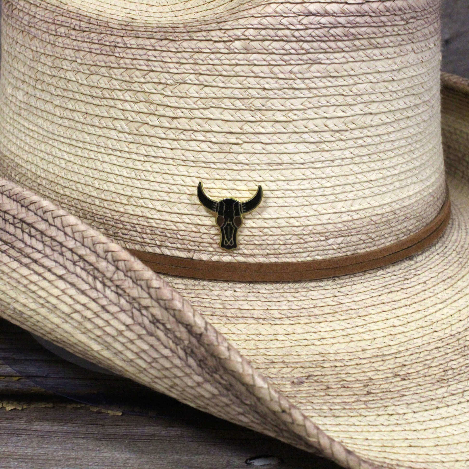 Close-up of a straw hat with a bull skull emblem on a wooden surface