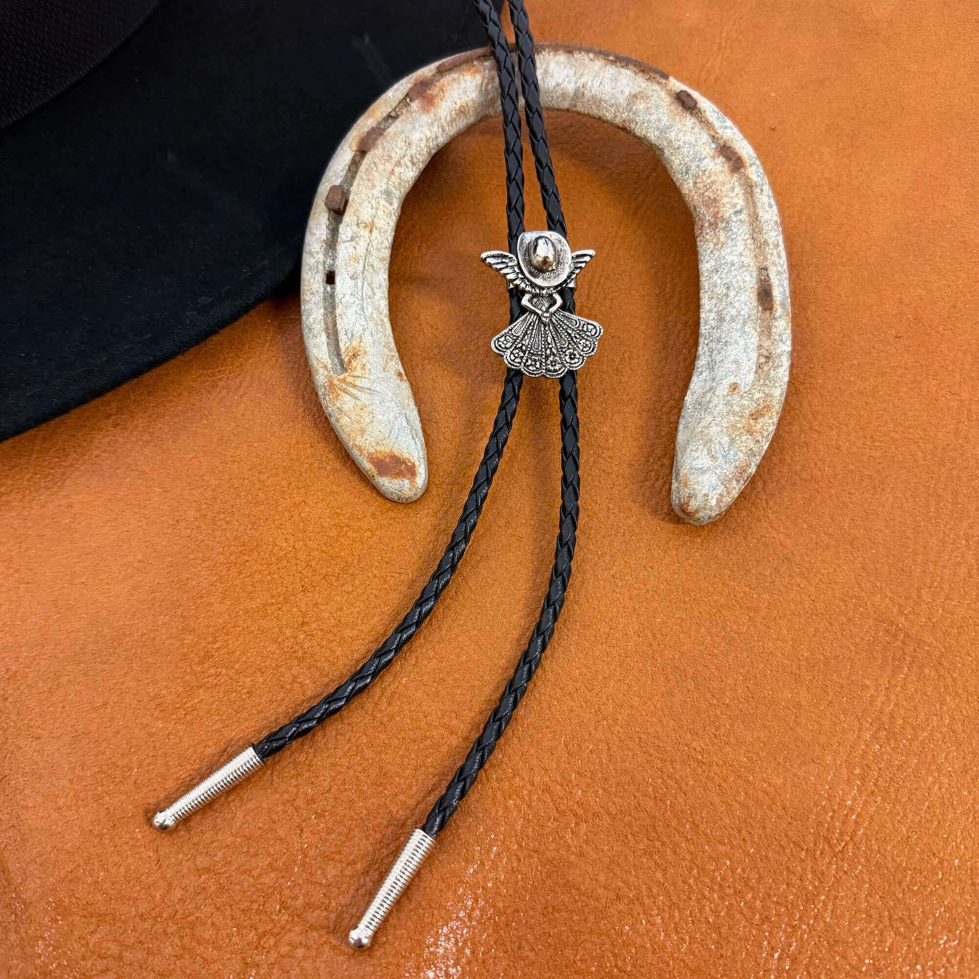 Horseshoe with angel charm and braided cord on a brown leather surface