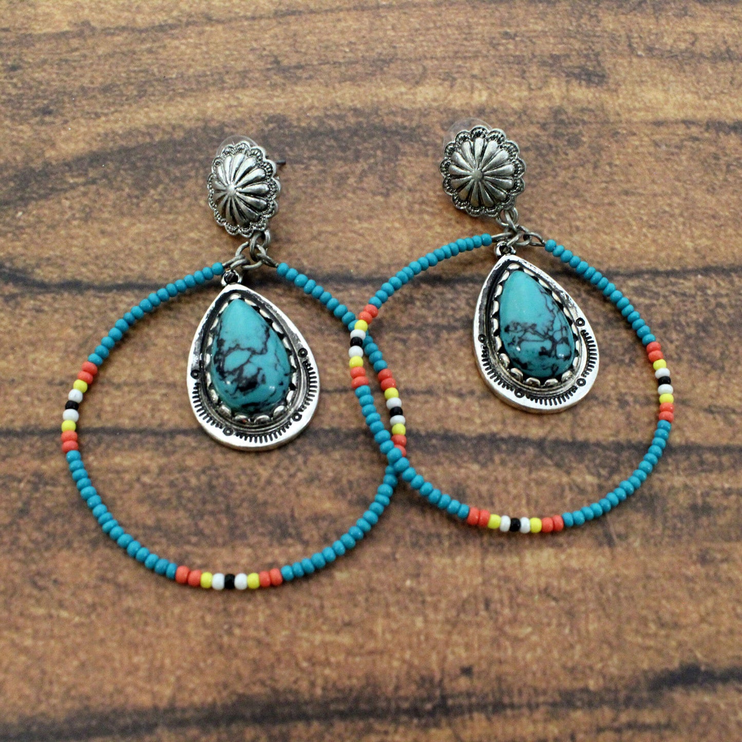 Pair of earrings with turquoise stones and colorful beading on a wooden surface