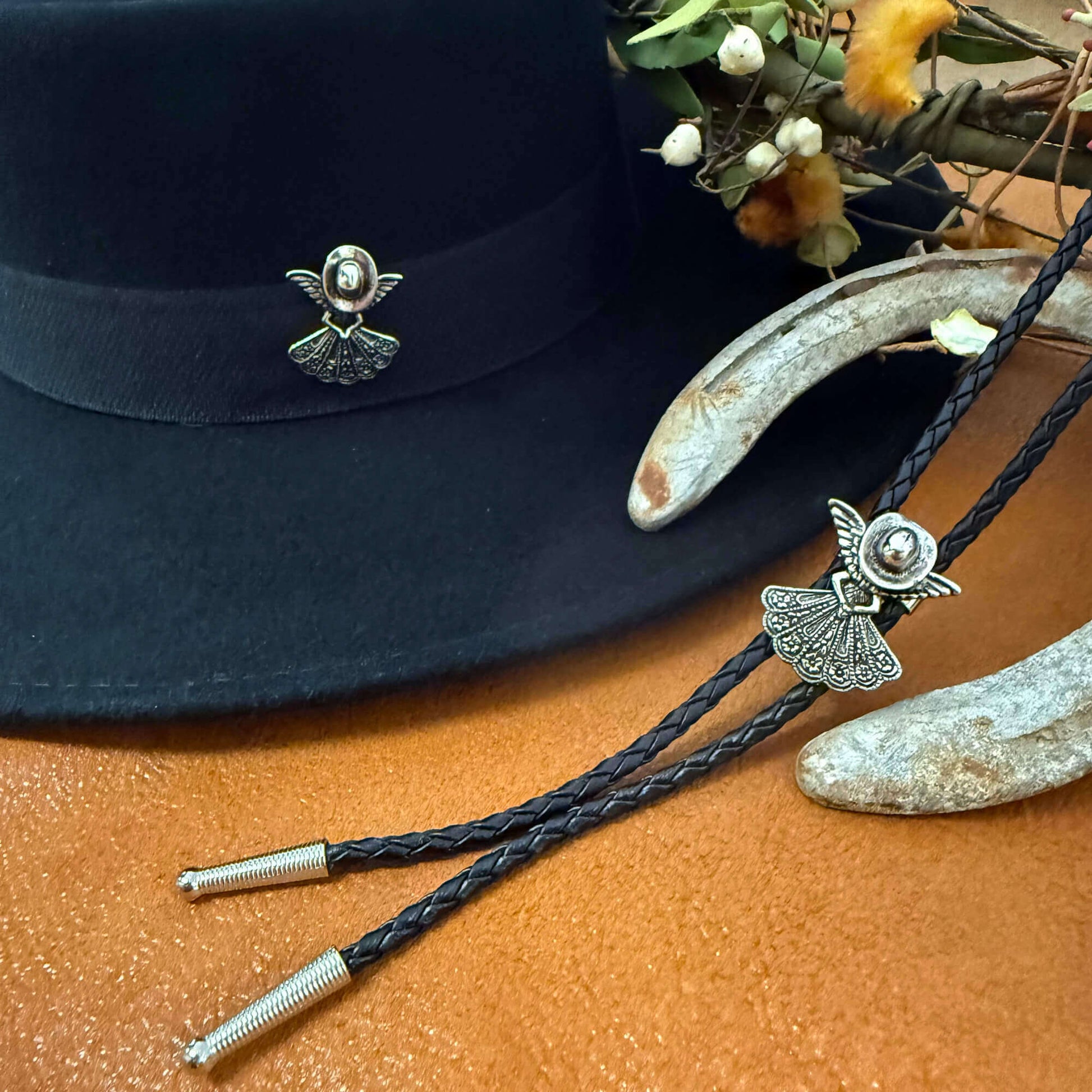 Black bolo tie with silver angel pendant on a black hat and wooden surface