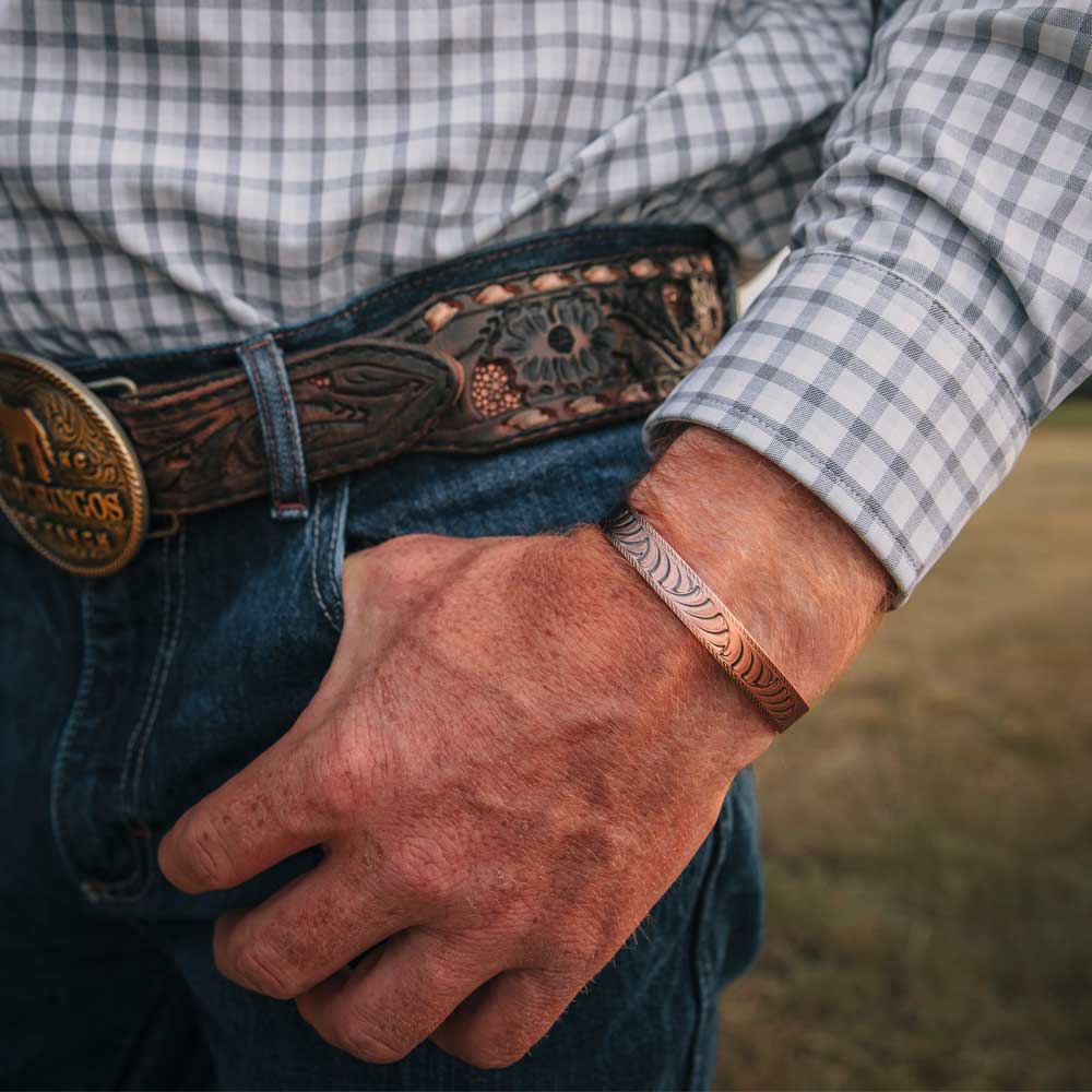 Close-up of a person wearing a checkered shirt, jeans, and a belt with a large buckle and matching bracelet.