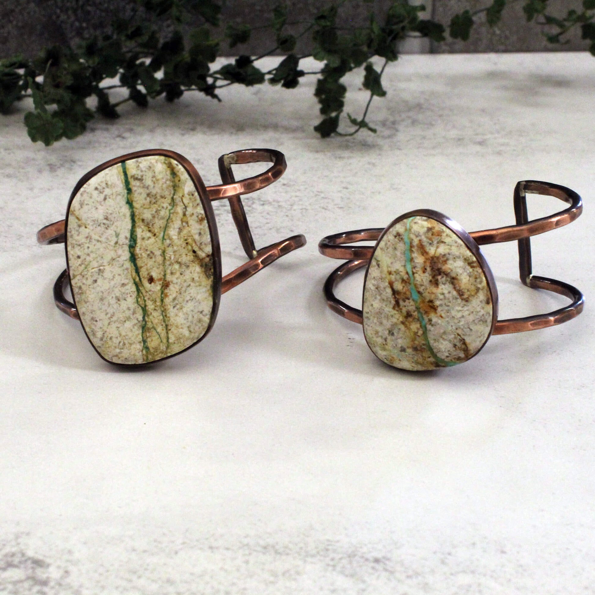 Two copper bracelets with stone-like oval stones on a textured surface.