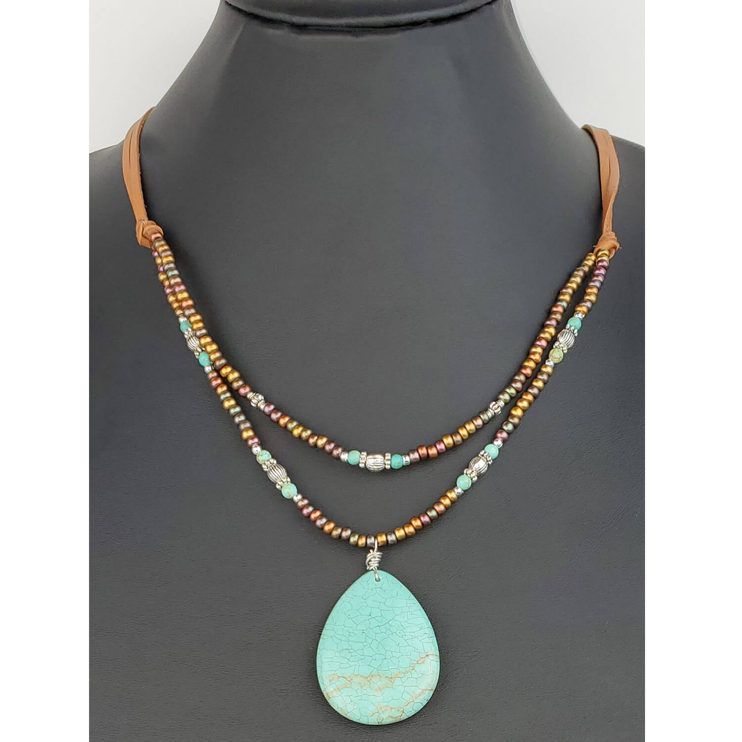 Handcrafted double strands of metallic bronze, silver and turquoise beads with a teardrop pendant 1.25″ by 1.75″ attached to tan leather cords. This stone helps you to calm and relax. Measures 23″ including a 4″ extender and lobster claw clasp. Each piece is unique and may vary slightly.