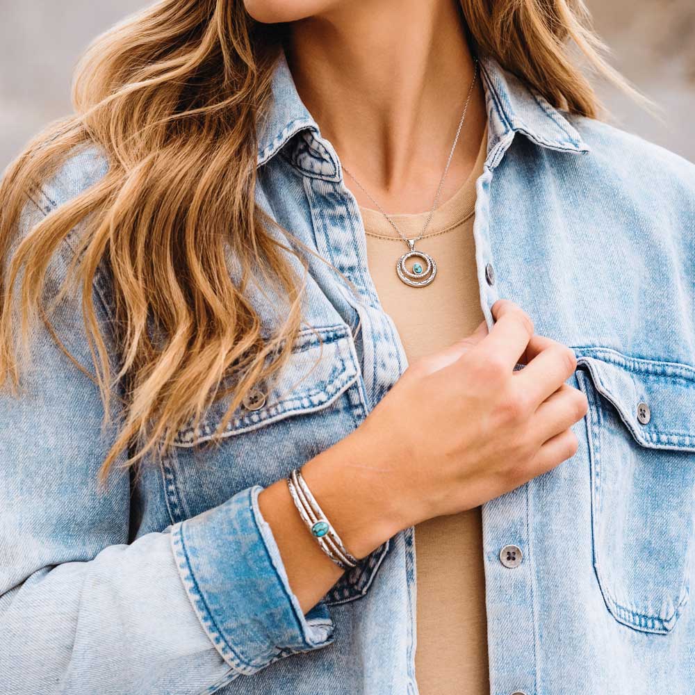 Woman wearing a denim jacket with a necklace and bracelet, outdoors.