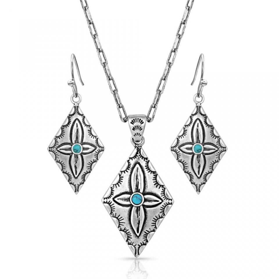 Silver-toned pendant-style jewelry set that includes earrings and a necklace. The earrings hang from a hypoallergenic French hook and are a diamond-shaped pendant with scalloped edges. An asymmetric flower sits in the center with a round turquoise stud. The necklace is the same diamond-shaped pendant, holding scalloped etching, and a flower with a turquoise center. It hangs from a 19" linked chain.